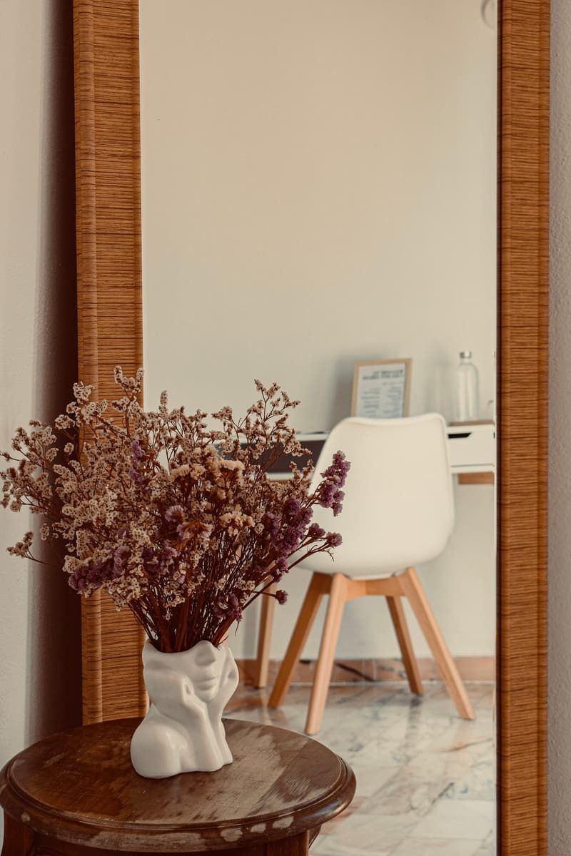 Mirror reflecting a dried flower arrangement and reading corner